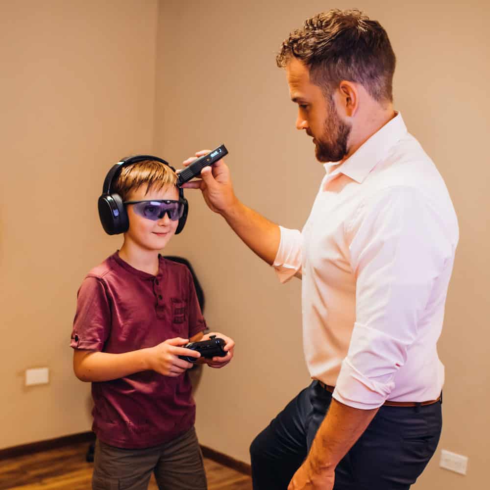 Dr. Sam using cold laser on child while the boy is playing videogame and wearing headphones.