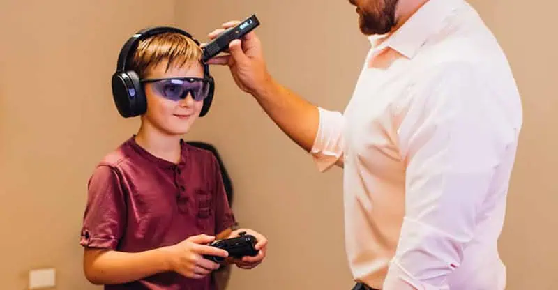 Dr. Sam using cold laser on child while the boy is playing videogame and wearing headphones.